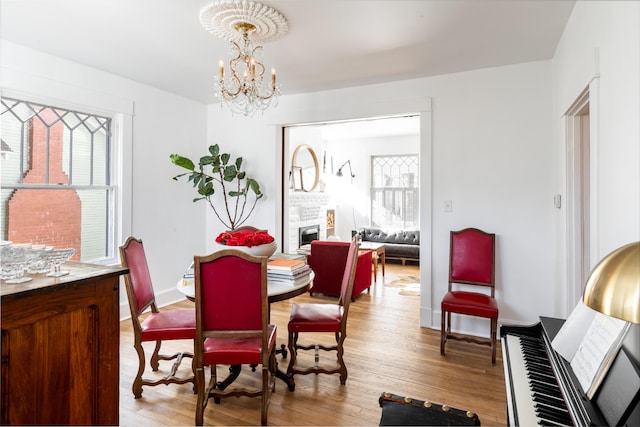 dining area featuring a brick fireplace, a notable chandelier, plenty of natural light, and light hardwood / wood-style floors