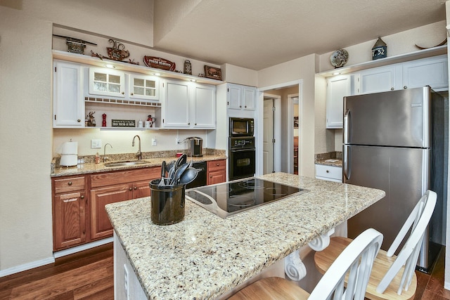 kitchen with a kitchen island, white cabinetry, sink, light stone counters, and black appliances