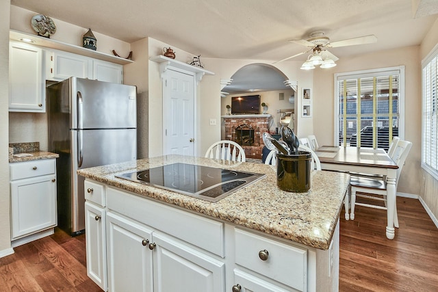 kitchen with white cabinetry, a center island, stainless steel fridge, dark hardwood / wood-style flooring, and black electric stovetop