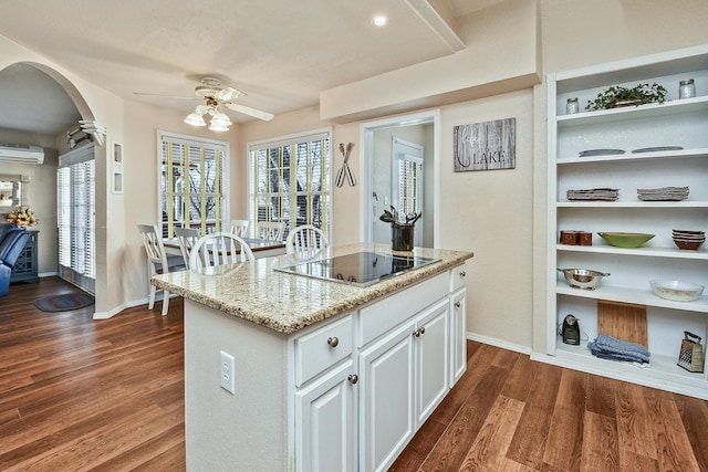 kitchen featuring white cabinetry, a wall mounted AC, light stone countertops, an island with sink, and black electric cooktop