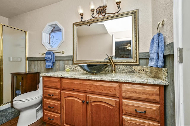 bathroom with an inviting chandelier, vanity, toilet, and a shower with door