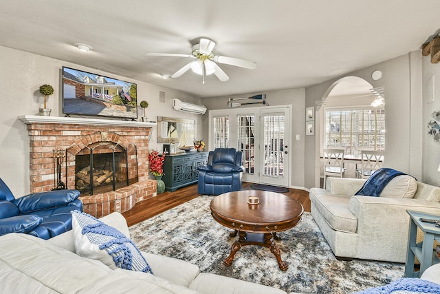 living room with hardwood / wood-style flooring, ceiling fan, an AC wall unit, and a fireplace