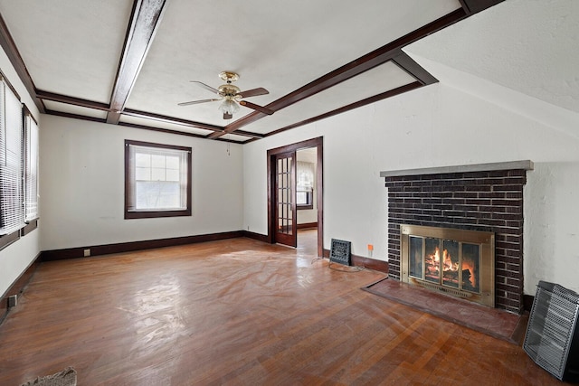 unfurnished living room with ceiling fan, wood-type flooring, beam ceiling, and a brick fireplace