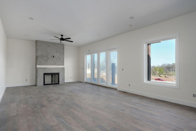unfurnished living room featuring wood finished floors, ceiling fan, baseboards, and a large fireplace