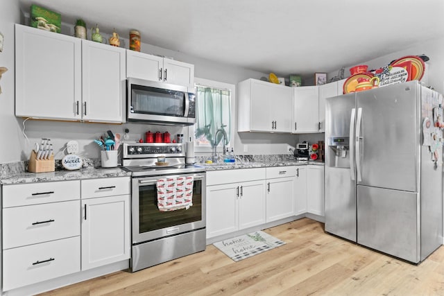 kitchen with sink, white cabinets, light stone counters, light hardwood / wood-style floors, and stainless steel appliances