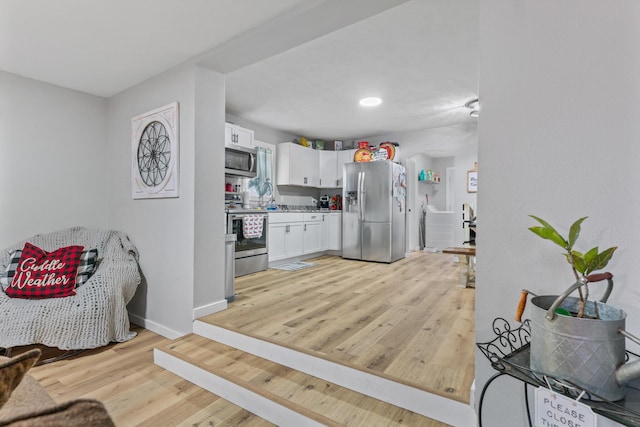 kitchen with stainless steel appliances, white cabinetry, and light hardwood / wood-style flooring