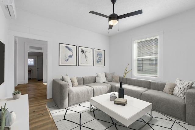 living room with ceiling fan, a wall mounted AC, a textured ceiling, and light wood-type flooring