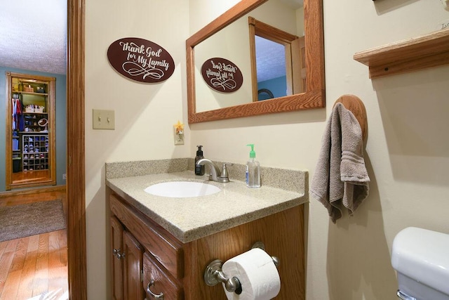 half bath with vanity, toilet, and wood finished floors