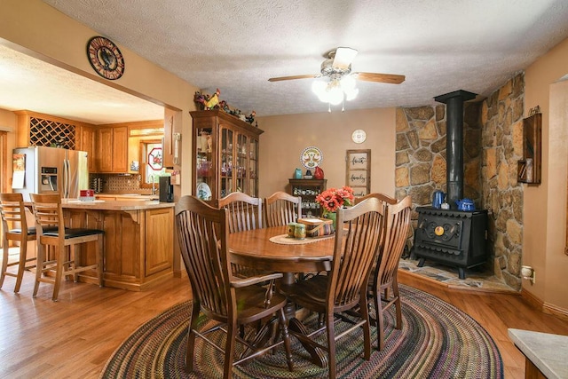 dining area with light hardwood / wood-style floors, a textured ceiling, and a wood stove