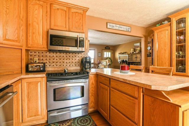 kitchen with wood-type flooring, a textured ceiling, appliances with stainless steel finishes, kitchen peninsula, and backsplash