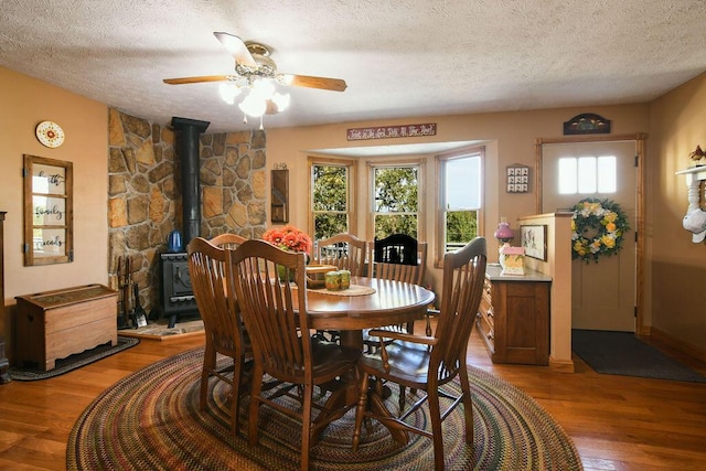 dining space with a ceiling fan, wood finished floors, a wood stove, and a textured ceiling