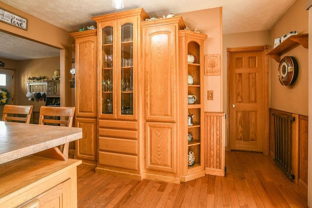 interior space with radiator heating unit, glass insert cabinets, light wood-type flooring, and a textured ceiling