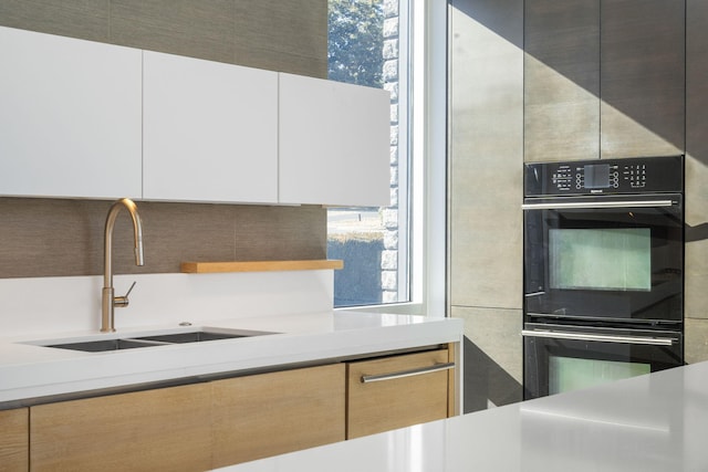 kitchen with black double oven, sink, and white cabinets