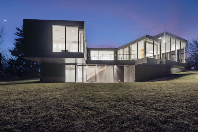 back house at dusk featuring a lawn