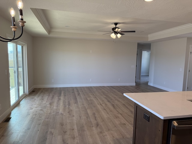 unfurnished living room with crown molding, a textured ceiling, ceiling fan with notable chandelier, a raised ceiling, and light wood-type flooring