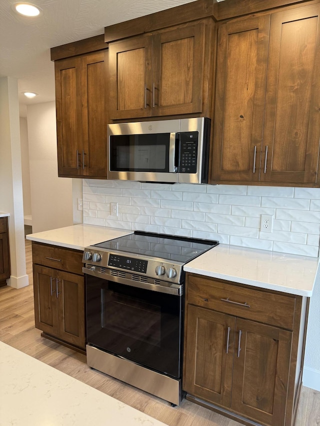 kitchen featuring stainless steel appliances, light stone countertops, light wood-type flooring, and decorative backsplash