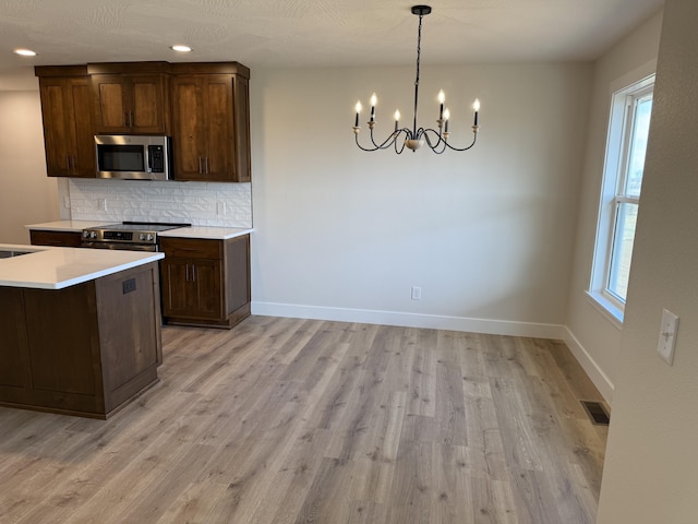 kitchen featuring pendant lighting, appliances with stainless steel finishes, tasteful backsplash, light hardwood / wood-style floors, and a healthy amount of sunlight