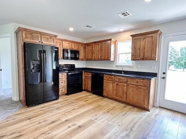 kitchen featuring sink, black appliances, light hardwood / wood-style floors, and a textured ceiling