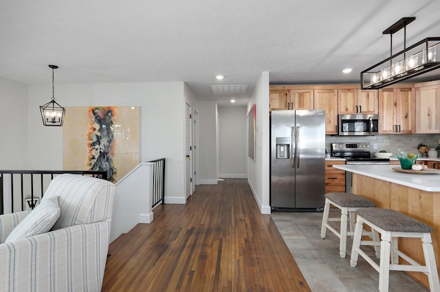 kitchen featuring a breakfast bar, backsplash, stainless steel appliances, dark hardwood / wood-style floors, and decorative light fixtures