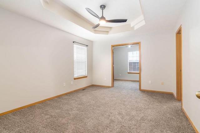 carpeted spare room with ceiling fan and a raised ceiling