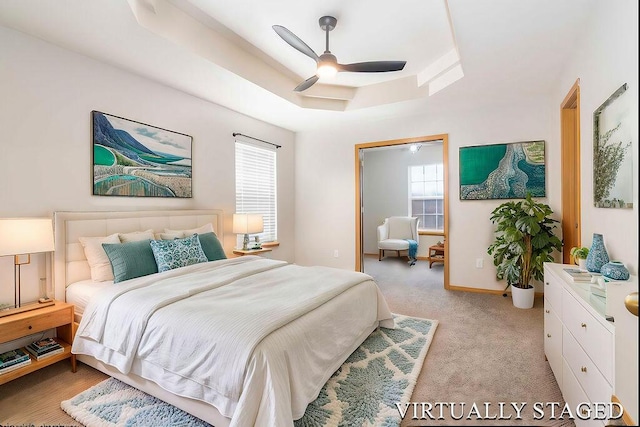 carpeted bedroom featuring multiple windows, a raised ceiling, and ceiling fan