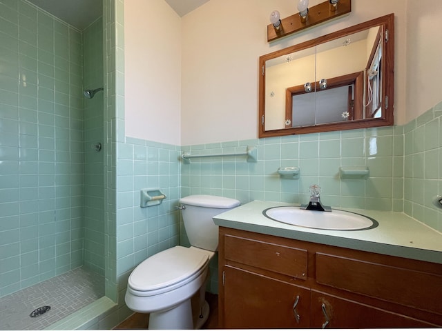 bathroom with a tile shower, tile walls, vanity, and toilet