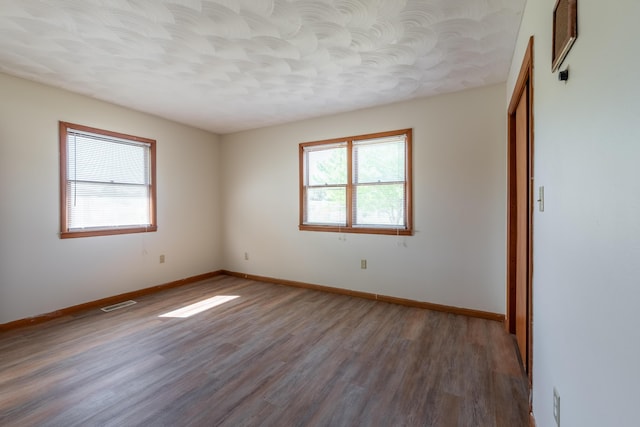 empty room with a textured ceiling, wood-type flooring, and a healthy amount of sunlight