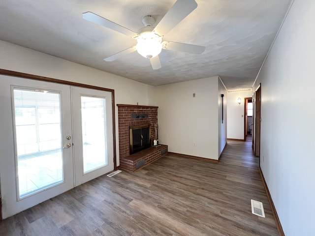 unfurnished living room featuring a brick fireplace, hardwood / wood-style flooring, french doors, and ceiling fan