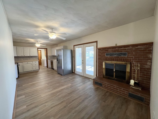 unfurnished living room with a fireplace, french doors, ceiling fan, and light wood-type flooring