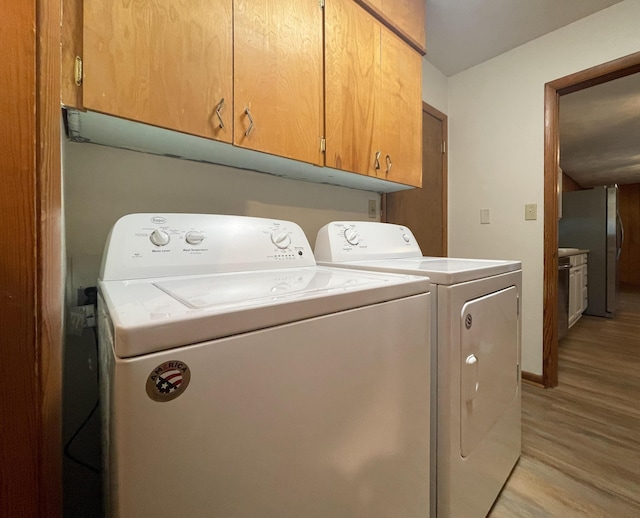 laundry area with cabinets, separate washer and dryer, and light hardwood / wood-style floors