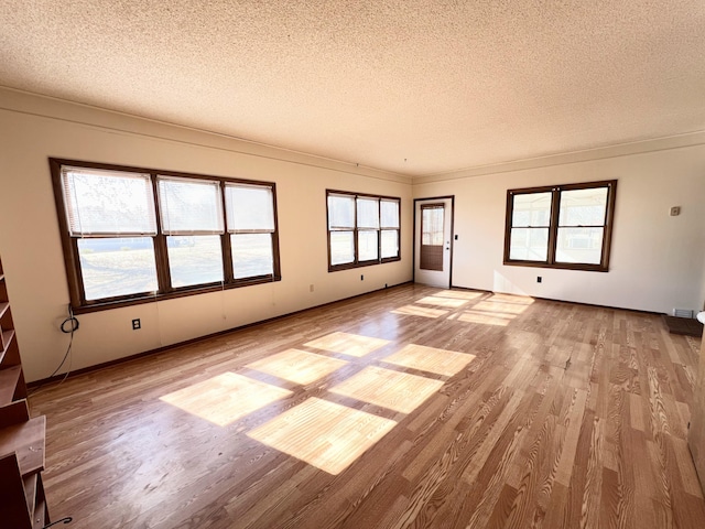 unfurnished living room featuring crown molding, a textured ceiling, and light wood-type flooring