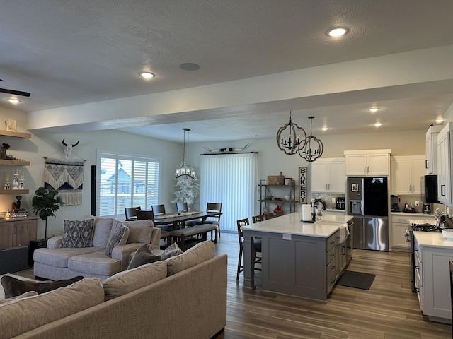 kitchen with appliances with stainless steel finishes, decorative light fixtures, white cabinetry, an island with sink, and an inviting chandelier