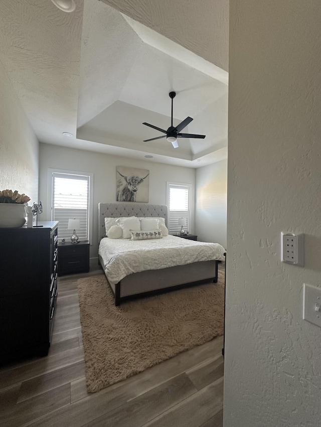 bedroom featuring hardwood / wood-style flooring, ceiling fan, a tray ceiling, and multiple windows