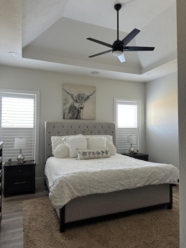 bedroom with a raised ceiling, dark wood-type flooring, and ceiling fan