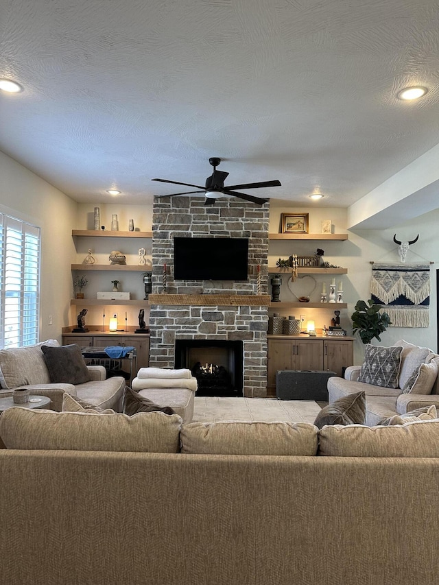 living room with ceiling fan, a textured ceiling, and a fireplace