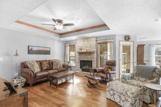 living room with a fireplace, ornamental molding, ceiling fan, a raised ceiling, and light wood-type flooring