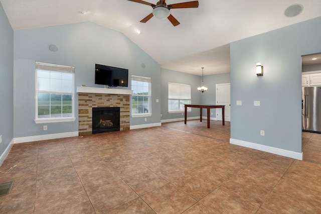 unfurnished living room with vaulted ceiling, a stone fireplace, ceiling fan with notable chandelier, and light tile patterned floors