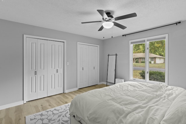 bedroom featuring ceiling fan, a textured ceiling, light hardwood / wood-style flooring, and two closets