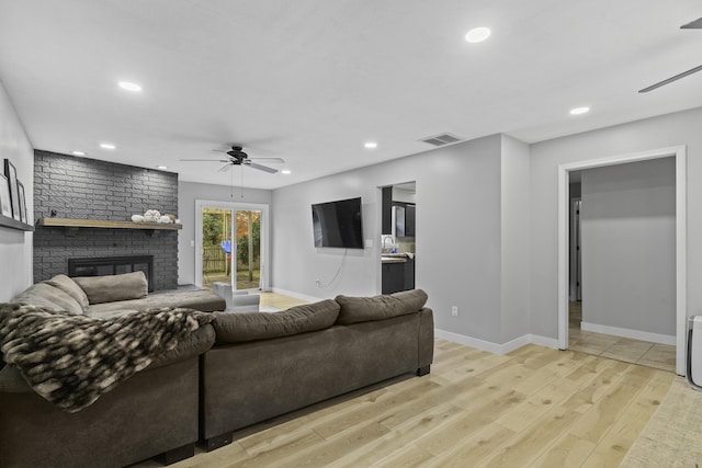 living room featuring ceiling fan, a brick fireplace, and light hardwood / wood-style flooring