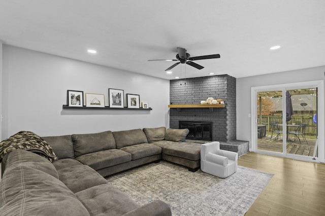 living room featuring hardwood / wood-style flooring, ceiling fan, and a brick fireplace