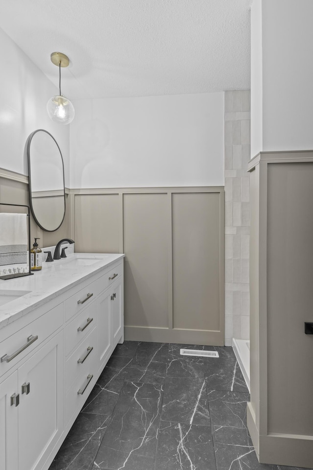 bathroom featuring tiled shower, vanity, and a textured ceiling