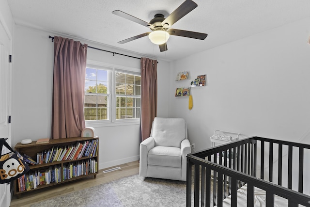 bedroom with a nursery area, ceiling fan, and wood-type flooring