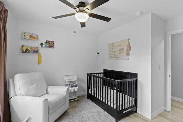 bedroom with light hardwood / wood-style flooring, a nursery area, and ceiling fan