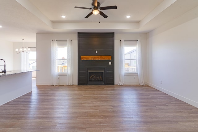 unfurnished living room featuring wood-type flooring, a large fireplace, a healthy amount of sunlight, and a tray ceiling