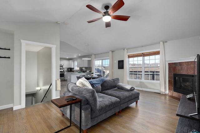 living room with vaulted ceiling, ceiling fan, a fireplace, and light hardwood / wood-style floors