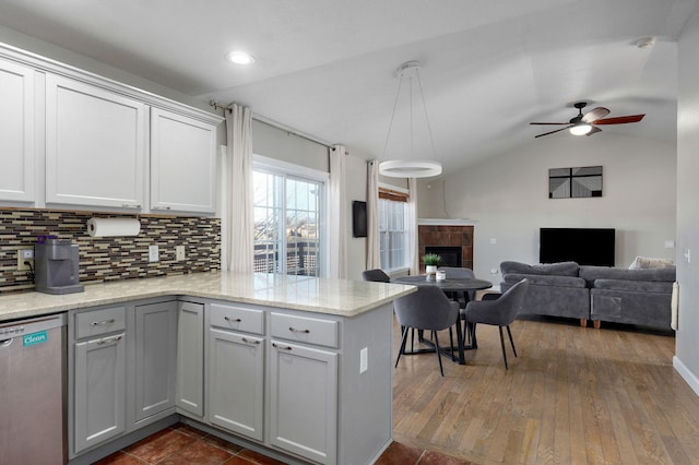 kitchen featuring pendant lighting, decorative backsplash, vaulted ceiling, stainless steel dishwasher, and kitchen peninsula