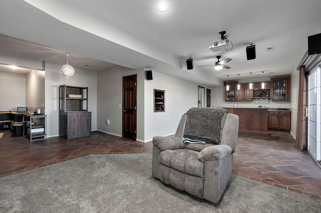 interior space with dark colored carpet, rail lighting, bar, and ceiling fan