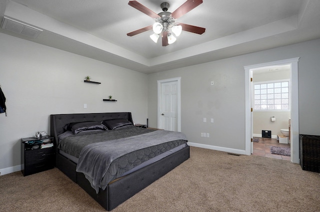 bedroom with light carpet, connected bathroom, a raised ceiling, and ceiling fan