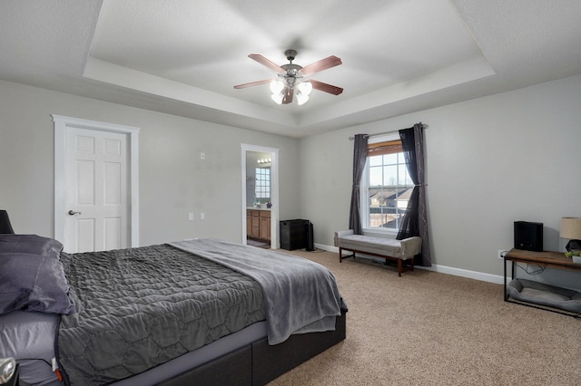 carpeted bedroom with a raised ceiling, ensuite bathroom, and ceiling fan