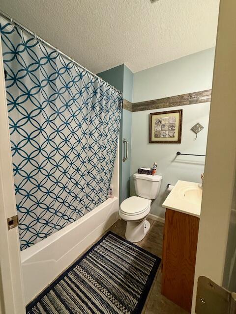 full bathroom with shower / tub combo with curtain, vanity, toilet, and a textured ceiling